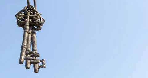 Three old rusty keys hang in the foreground against a blue sky Stock Photos