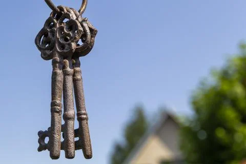 Three old rusty keys hang in the foreground against a blue sky Stock Photos