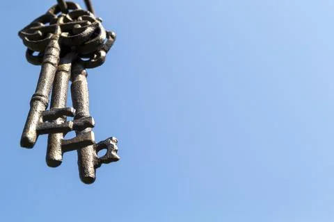 Three old rusty keys hang in the foreground against a blue sky Stock-Fotos