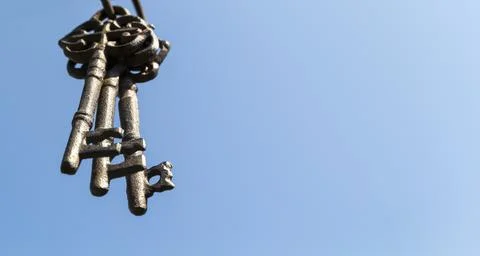 Three old rusty keys hang in the foreground against a blue sky Stock Photos