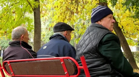 Three older men sitting on bench in park and talking, old age, autumn weather. Stock Footage 56324910