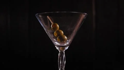 Three olives on a toothpick fall into an empty Martini glass on a wooden table. Stock Footage 164350476