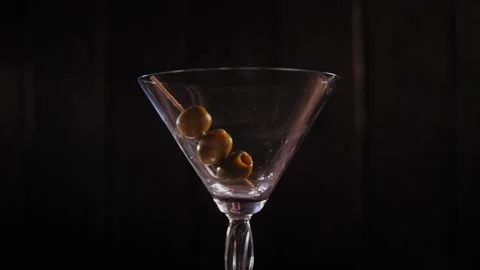 Three olives on a wooden toothpick fall into an empty Martini glass. Stock Footage 145134041