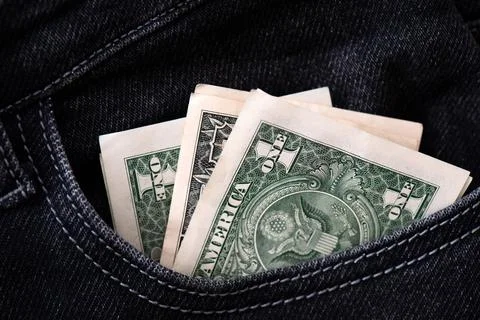 Three one dollar banknotes stick out in the pocket of black jeans. Stock Photos