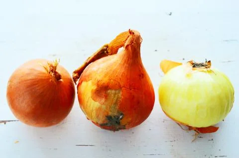 Three onions on a white table Stock Photos