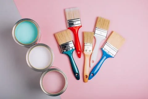 Three open cans of pastel paint with five brushes on pink and grey background. Stock Photos