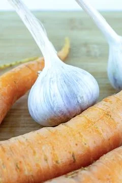Three orange carrots, part of root vegetable and a pair of garlic close-up Stock Photos