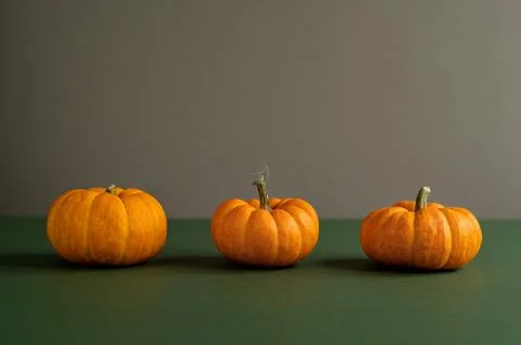 Three orange pumpkins arranged on a green surface in row with copy space. Stock Photos