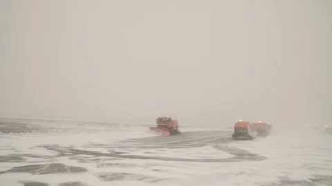 Three orange snow plows are cleaning snow from the airport landing path at Stock Footage 102485775
