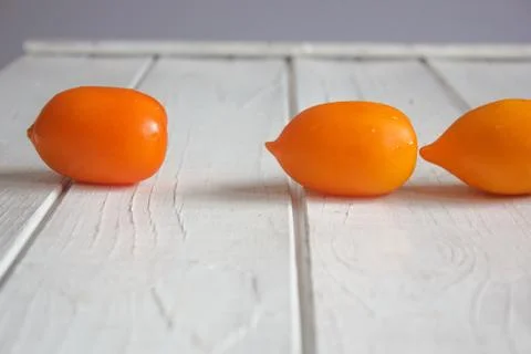 Three orange tomatos on white wooden board Stock Photos