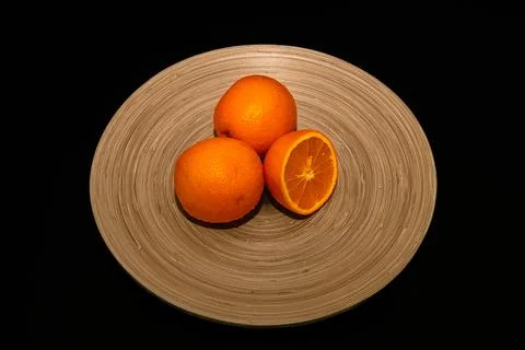 Three oranges on a plate with one cut in half Stock Photos