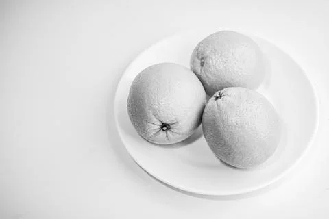 Three oranges in a plate on a white background. Black and white photo. Still Stock Photos