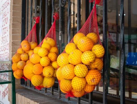 Three packaging nets with oranges hanging on a window steel bars for selling Stock Photos