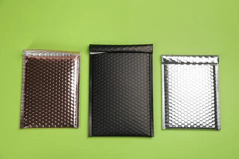 Three padded envelopes with bubble wrap on green background, flat lay Stock Photos