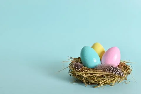 Three painted eggs lie in a nest on a pale blue background. Stock Photos