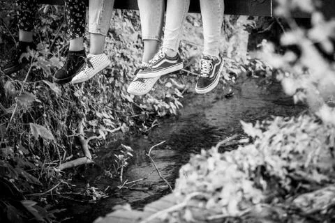 Three Pairs Of Legs Dangle From A Bridge Over A Small Stream Stock Photos