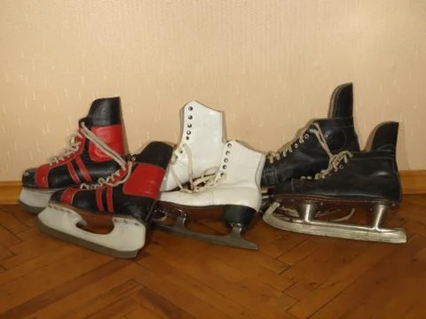 Three pairs of old skates lying on the parquet floor Stock Photos