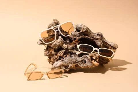 Three pairs of sunglasses displayed on driftwood on beige background Stock Photos