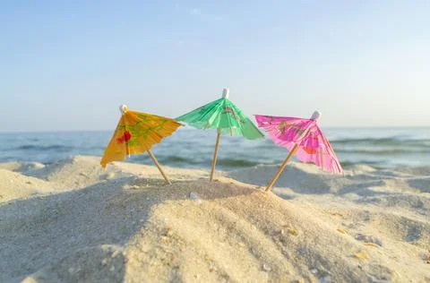 Three paper cocktail multi-colored umbrellas on sandy sea beach with blue sky Foto stock