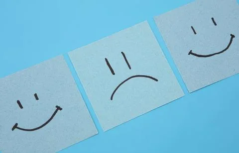 Three paper notes with happy and sad face drawings on blue background Stock Photos