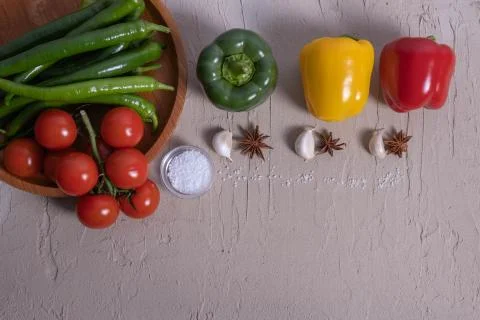Three paprika, different vegetables and spices lie on a table and a wooden tr Stock Photos