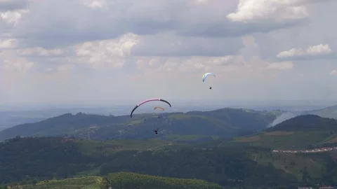 Three para gliders gracefully floating over green landscape &amp; cloudy skies Stockbeeldmateriaal 102065036