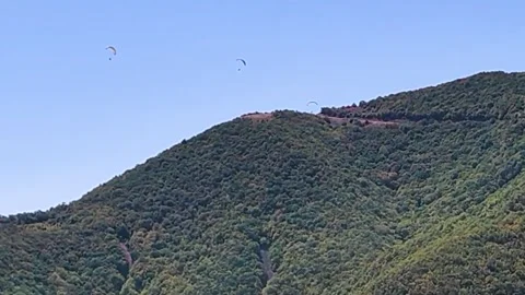 Three Paragliders Flying Above Green Mountain Ridge Under Clear Blue Sky 動画素材 345289072