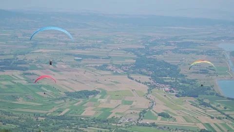 Three Paragliders Soar Over Green Hills and Farmland Stock Footage 304676304