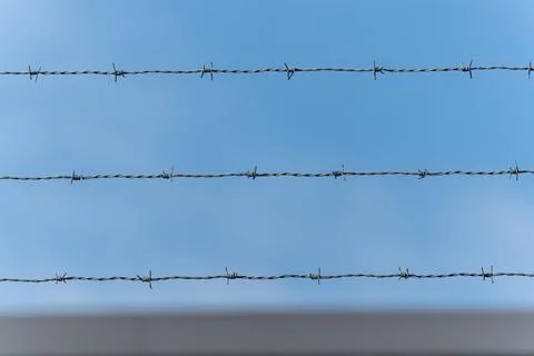 Three parallel barbed wire strands stretch across a clear blue sky Stock Photos