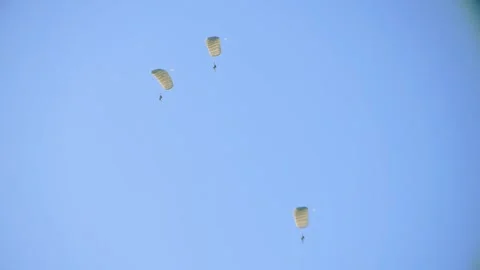 Three paratroopers descend under open parachutes in a clear blue sky, Video stock 286295080
