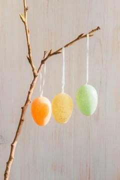 Three pastel-colored Easter eggs on tree branch on vintage wood background Stock Photos