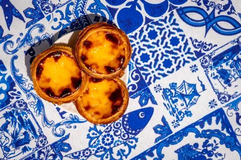 Three pastel de nata custard tarts overhead on blue and white tablecloth Stock Photos