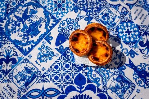 Three pastel de nata egg tarts overhead on blue and white tile tablecloth Stock Photos