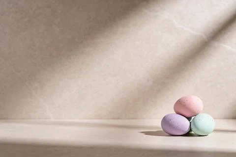 Three pastel Easter eggs stacked on a neutral surface with dappled light sh.. Stock Photos