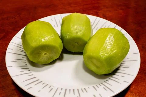 Three peeled kiw ifruits on a patterned white plate on wooden table, close-up. Stock Photos