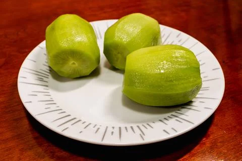 Three peeled kiw ifruits on a patterned white plate on wooden table, close-up. Foto stock