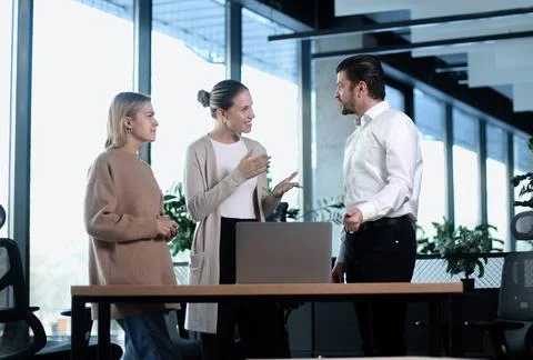 Three people are standing around a desk in a business setting Stock Photos