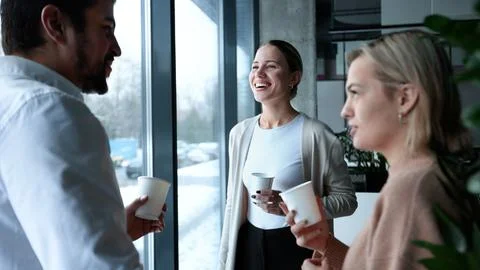 Three people are standing in front of a window, smiling and holding cups Stock Photos