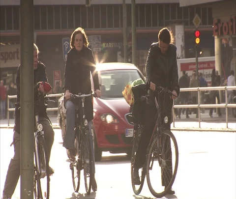 Three people on bicycles waiting at traffic light, they ride when light changes Stock-Footage 86742939