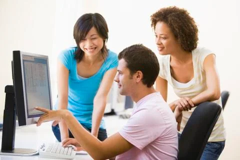 Three people in computer room pointing at monitor and smiling Stock Photos