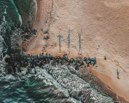 Three people facing rolling waves of sea on a clean wide sandy beach during m Stock Photos