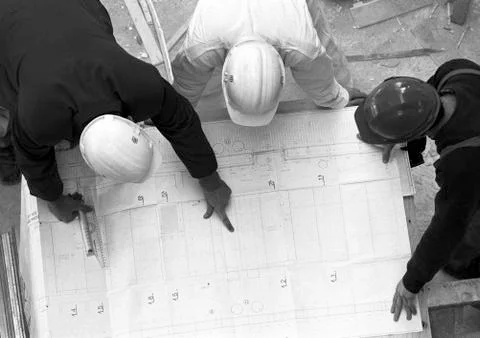 Three people with hard hats, examining blueprint, elevated view, b&w Stock Photos