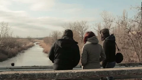 Three people looking down the river standing on a bridge. Cold winter weather Stock Footage 84836402
