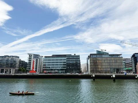 Three people rowing on the river in front of modern glass office buildings .. Photos