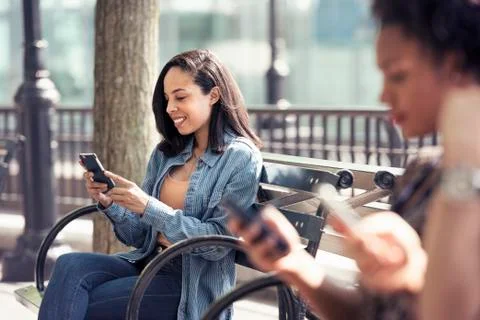 Three people seated side by side on a park bench checking their smart phones Stock Photos