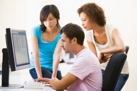 Three people sitting in computer room looking at monitor Stock Photos