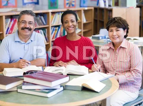 Three people sitting in library with books and notepads (selective focus) Stock Photos