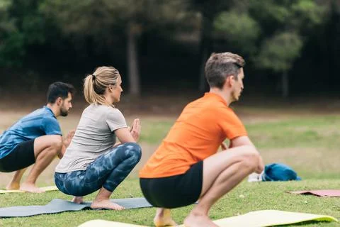 Three people squatting while doing yoga in a park Stock Photos