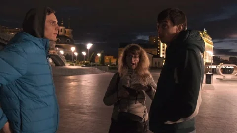 Three people stand in the night in the middle of the square and talking Видео 132729411