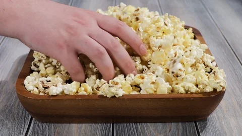 Three people take turns picking a handful of popcorn from a large wooden plat Vídeos de archivo 113689335